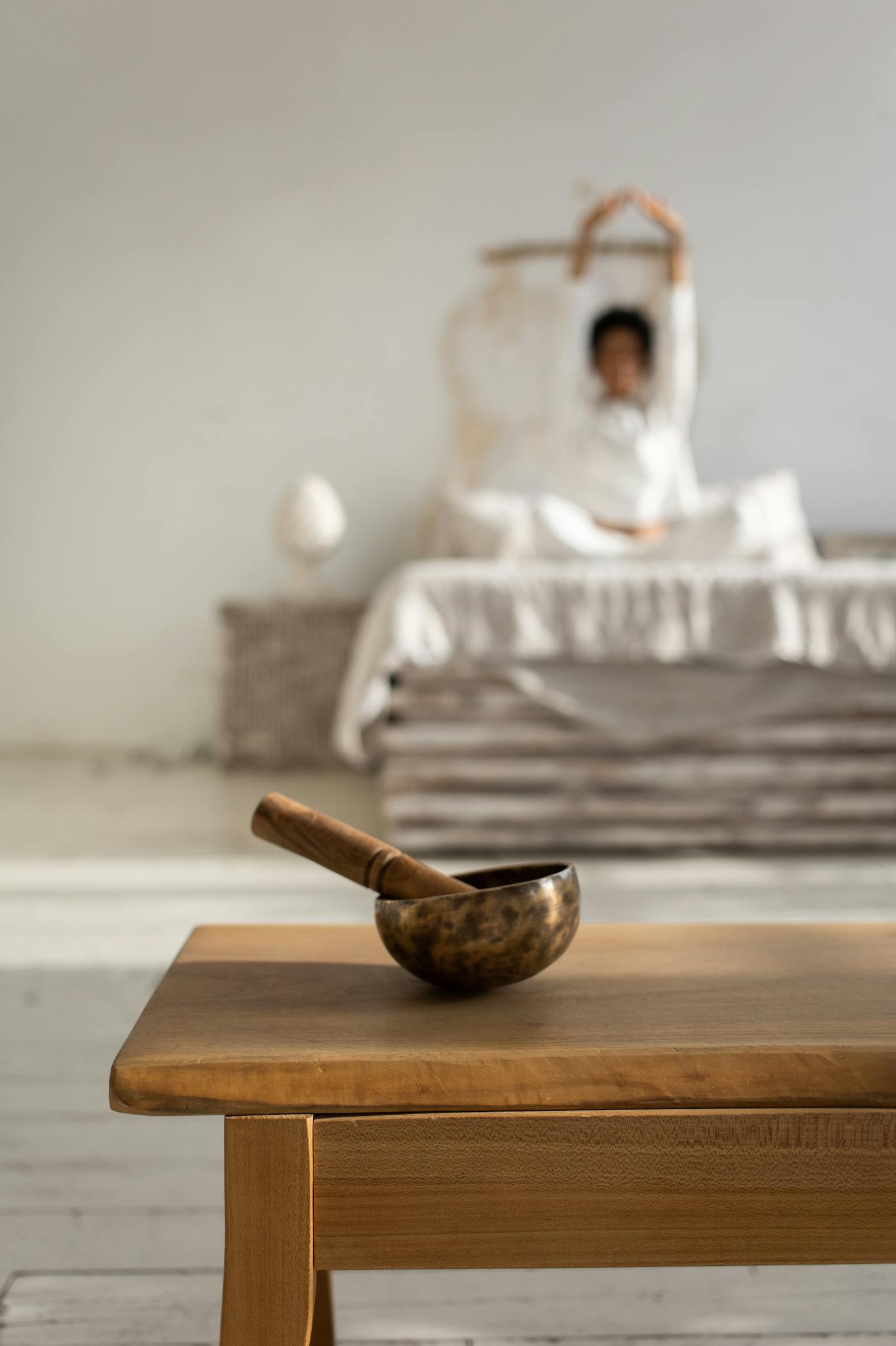 A peaceful setting featuring a singing bowl and a person stretching on a bed.