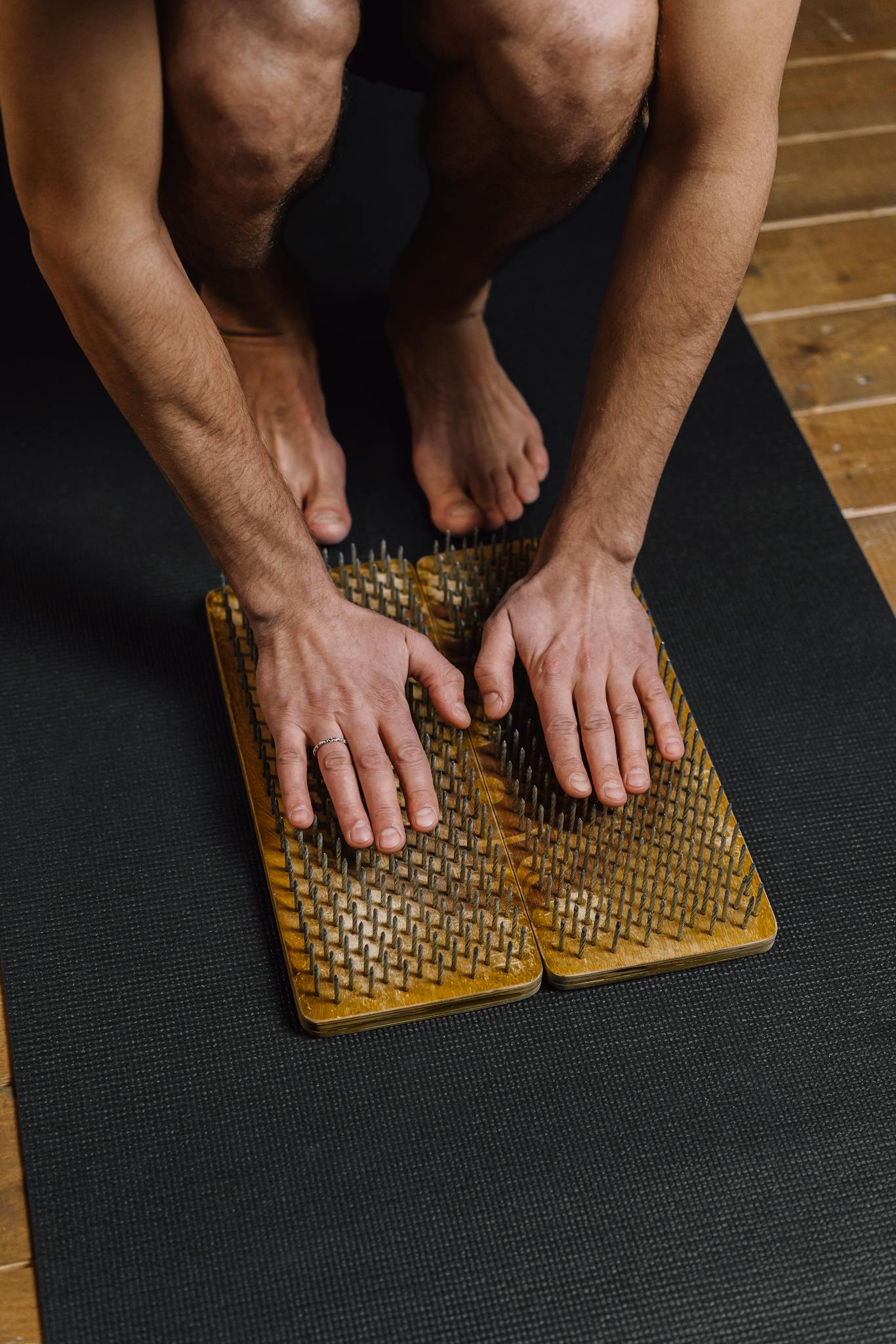 Man practicing meditation with hands on a wooden spike board for therapeutic relaxation indoors.